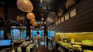 Un restaurante con interior de madera, un mostrador de buffet con diversos platos y lámparas colgantes de tejido.