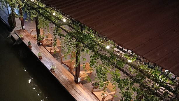 Terraza de madera con sillas y plantas en macetas, con vista a un cuerpo de agua.