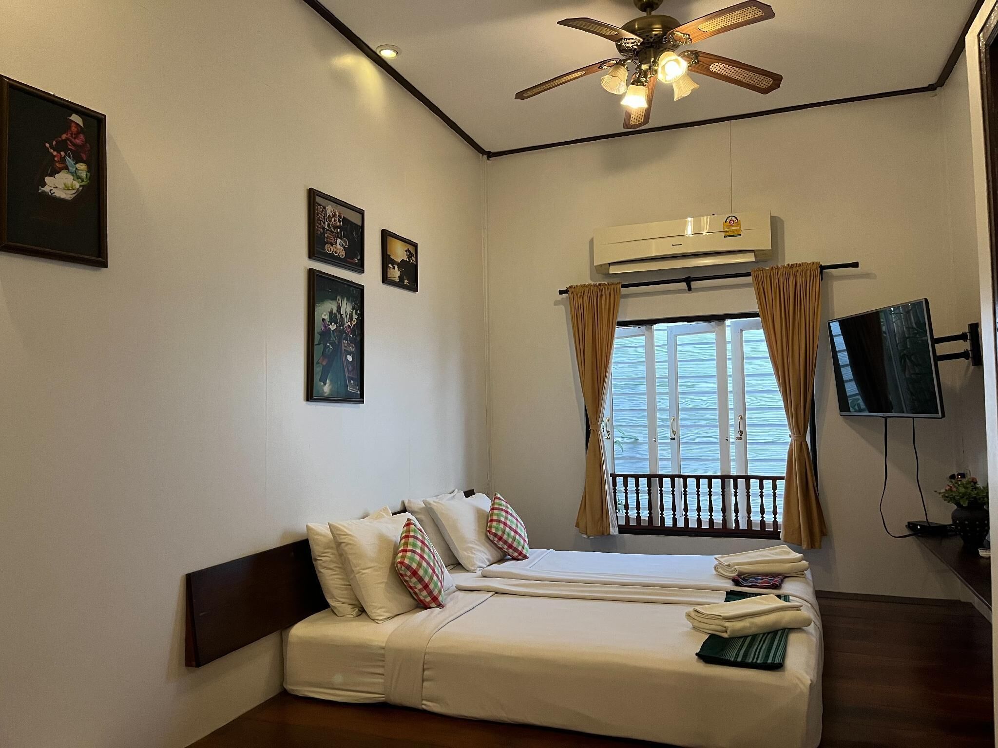A hotel room with a bed, a ceiling fan, an air conditioning unit, a television, and artwork on the wall.