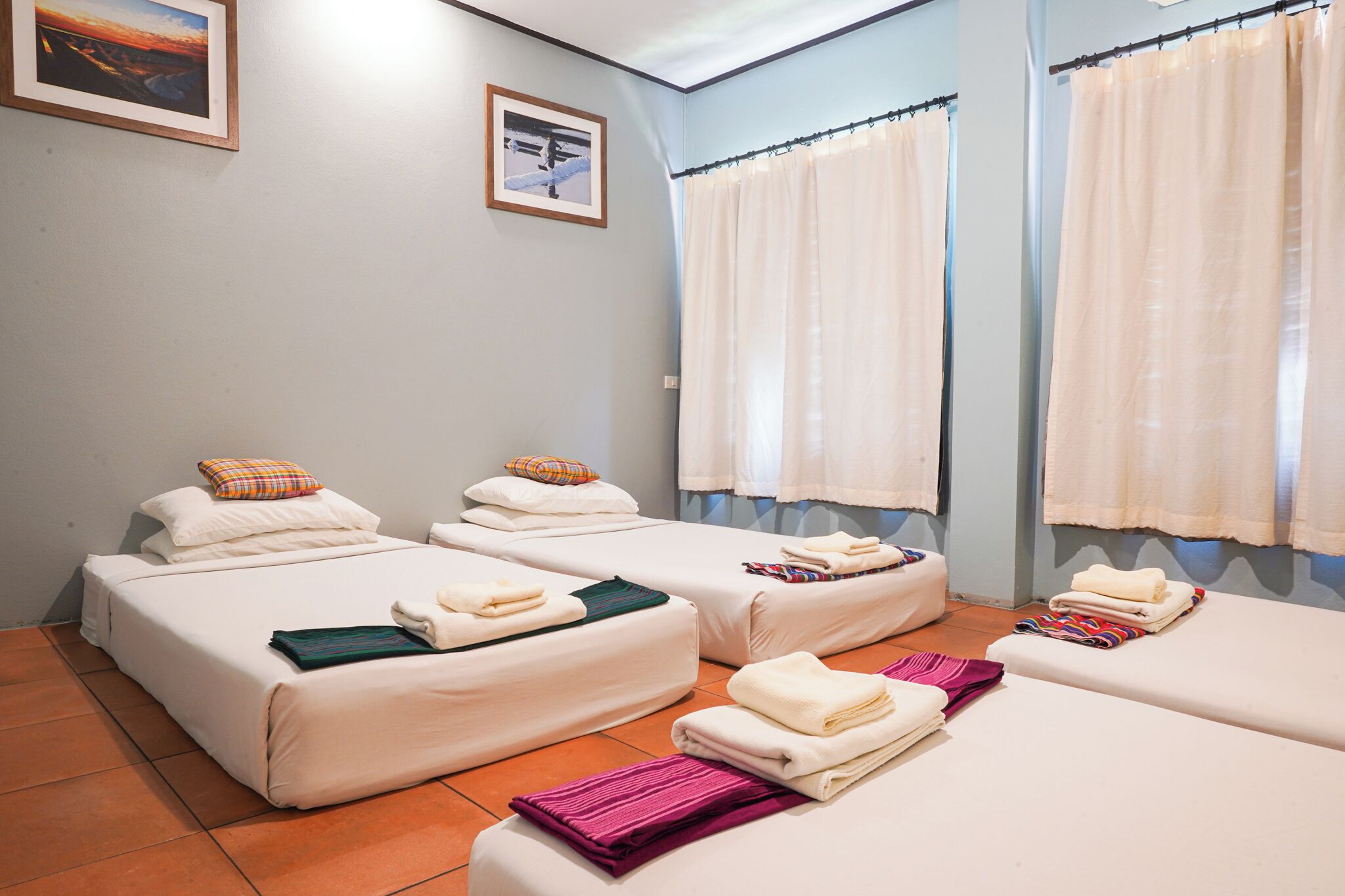 A hotel room with three beds, each with a pillow and a folded towel.