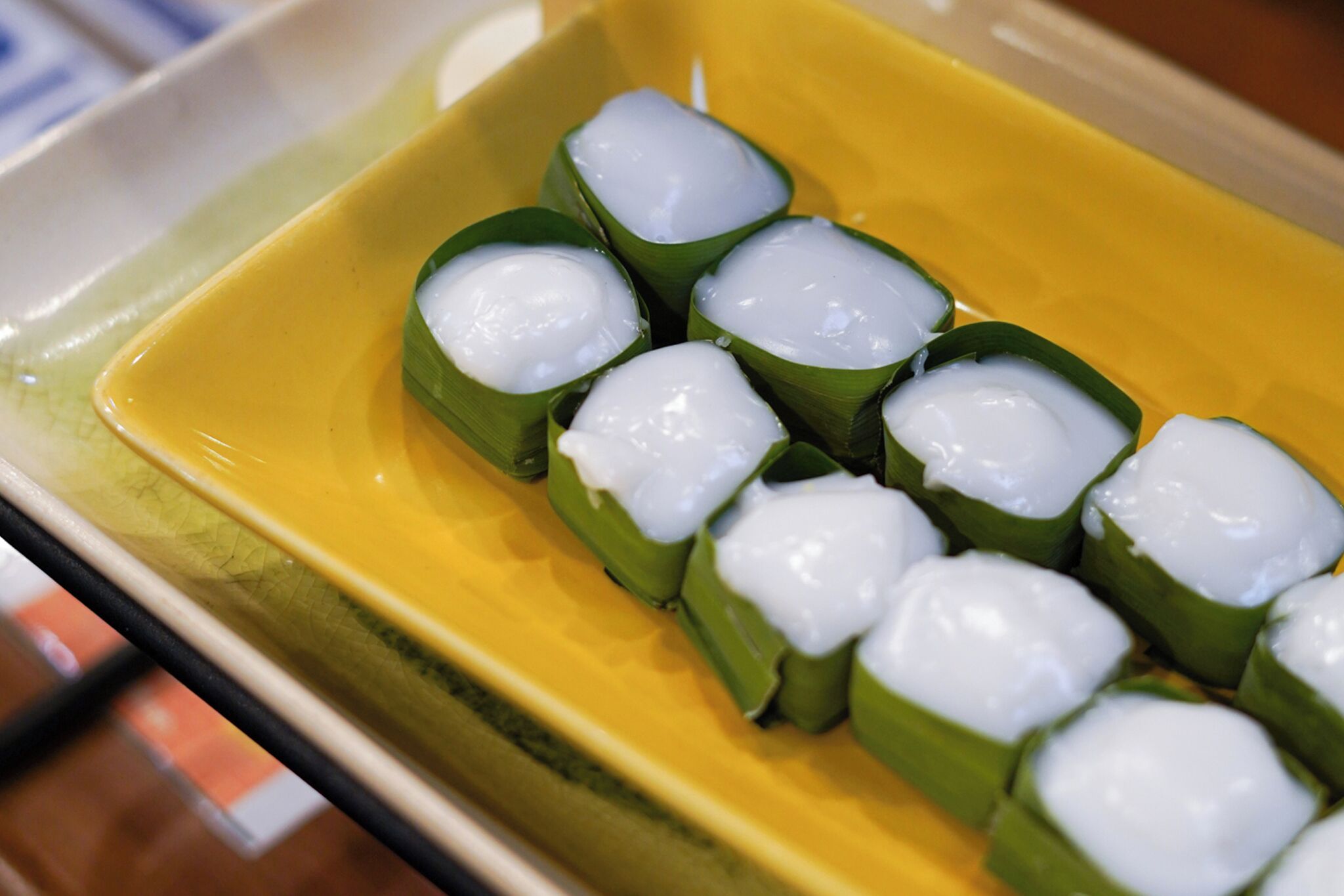 A yellow rectangular plate with several food items wrapped in green leaves.