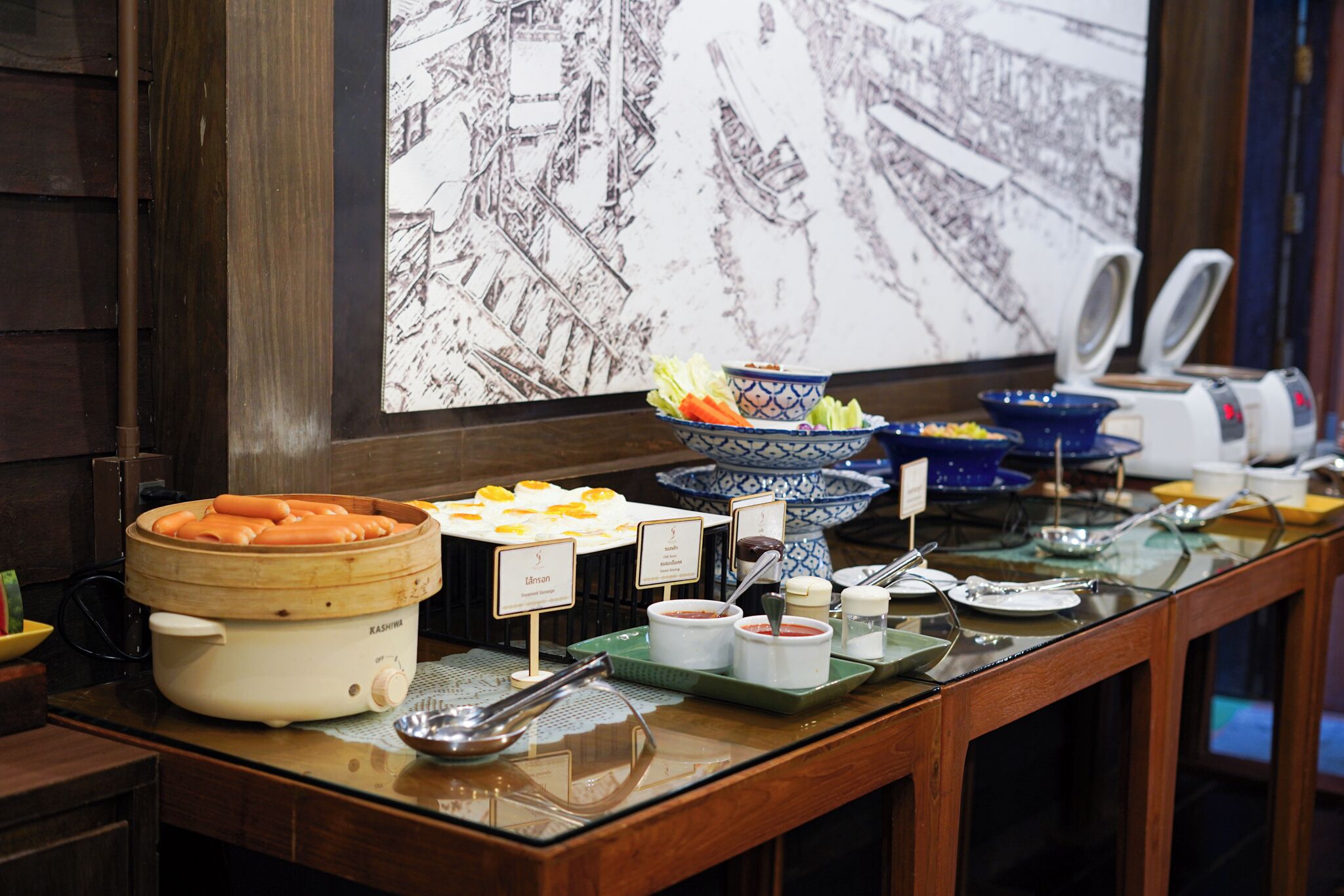 A buffet setup with various food items and condiments, including a steamer, bowls, and a blue and white ceramic dish.