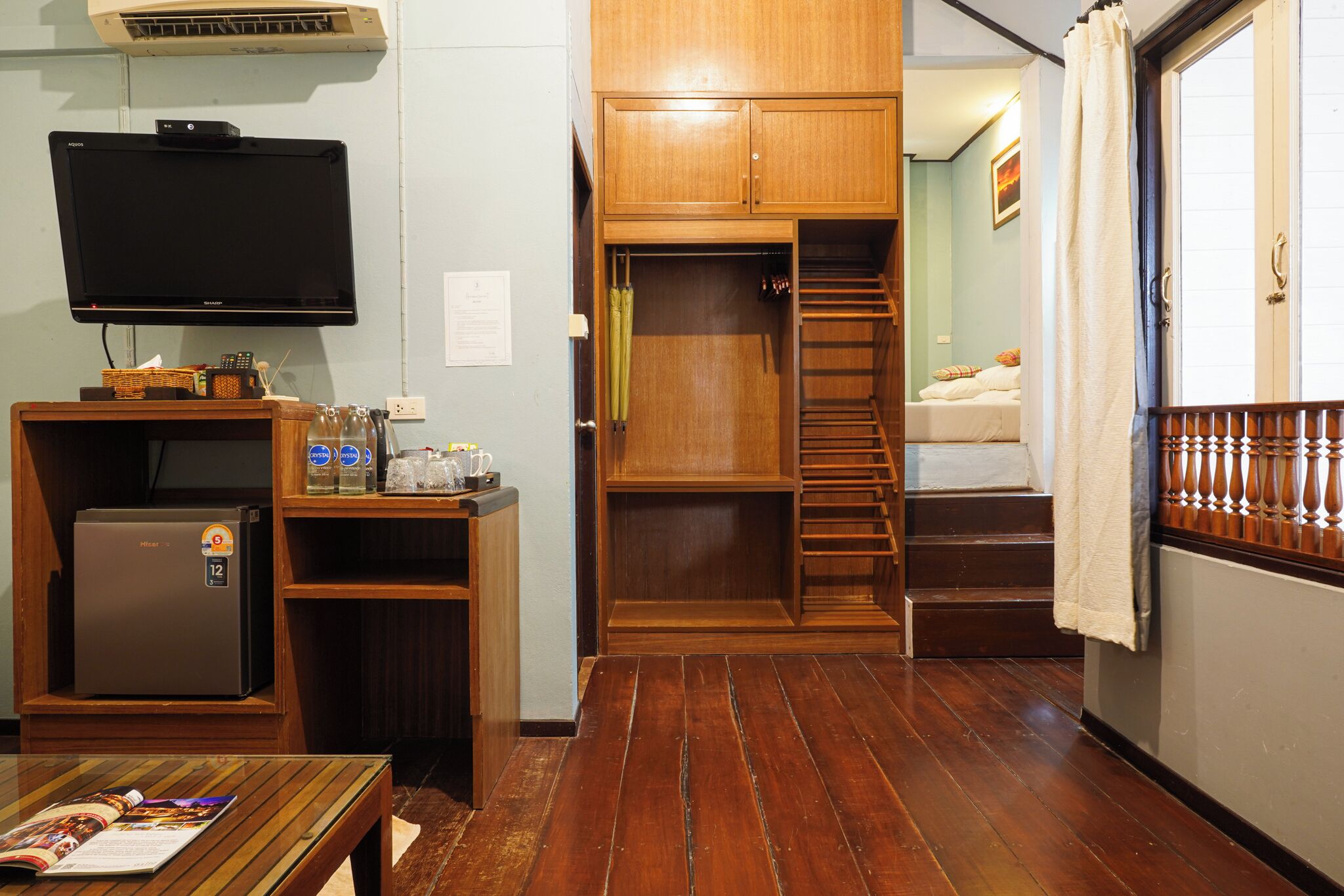 A compact room with a built-in TV, a small refrigerator, a wooden desk, and a staircase leading to a bed.