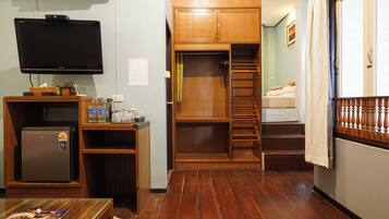 A compact room with a built-in TV, a small refrigerator, a wooden desk, and a staircase leading to a bed.