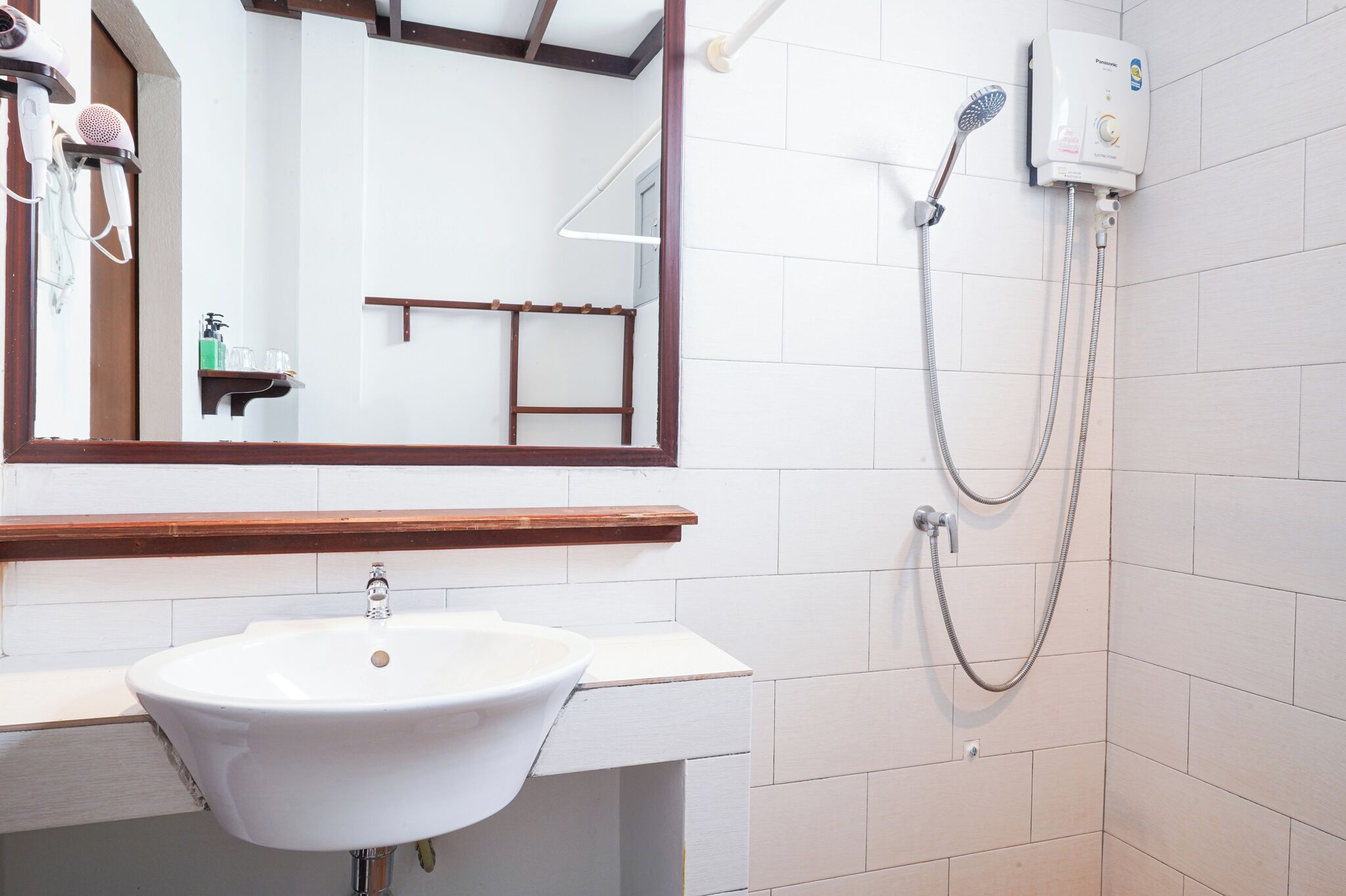 A bathroom with a white sink, a mirror, a handheld showerhead, and a wall-mounted faucet.