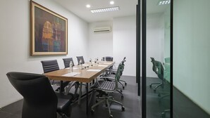 Un salón de conferencias con una larga mesa, sillas negras y un cuadro grande en la pared.