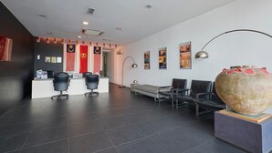 Un área de recepción moderna con un mostrador, sillas de cuero negro, un gran jarrón decorativo y banderas de Malasia.