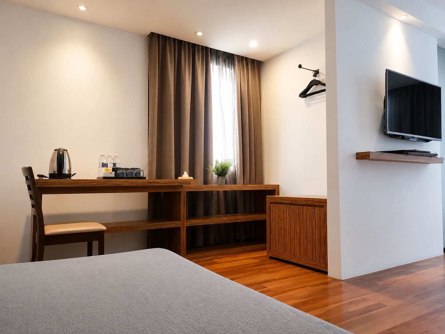 A modern hotel room with a wooden desk, a chair, a bed, a TV, and a small plant.