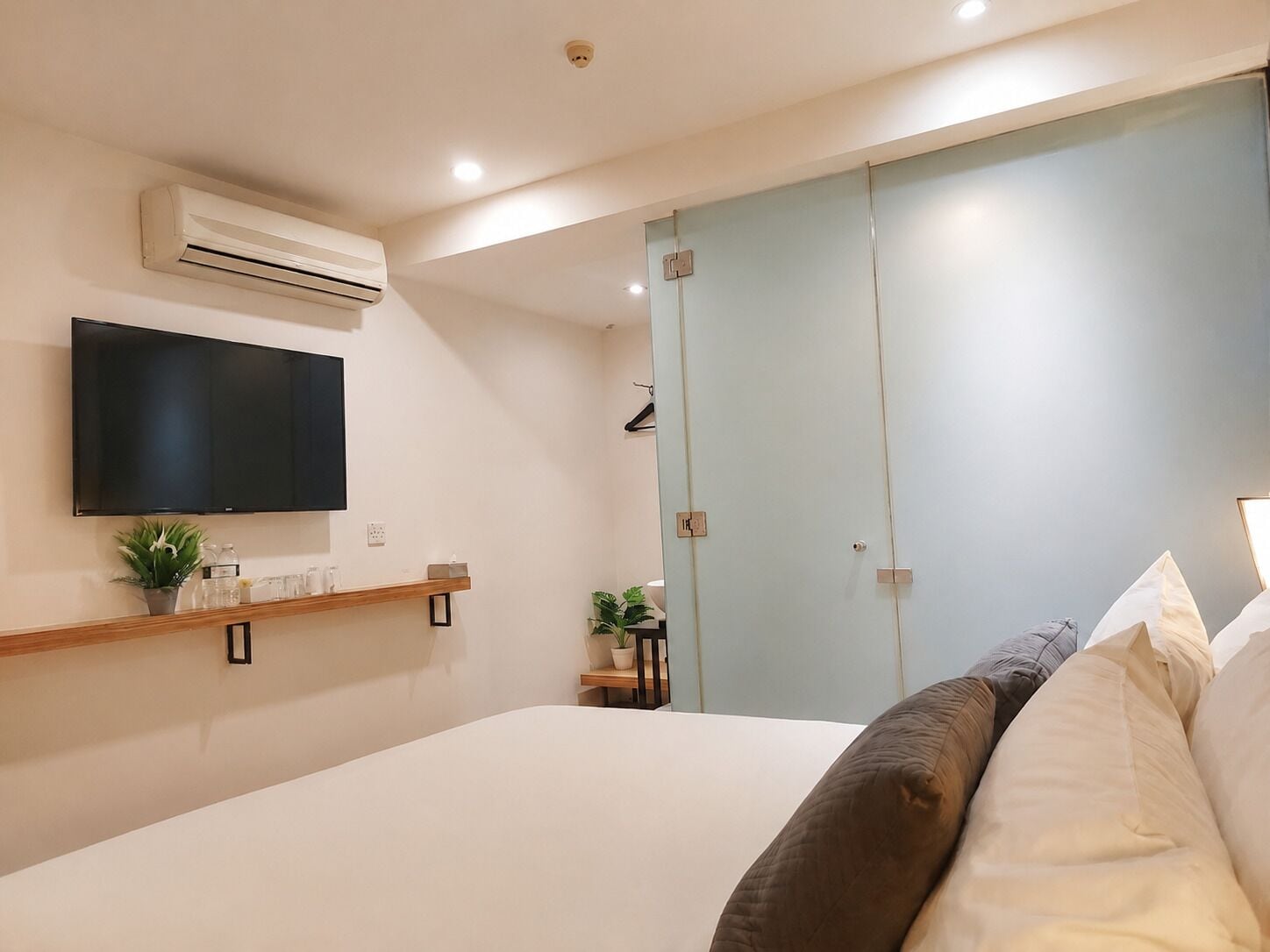 Een slaapkamer met een bed, een wandtelevisie, een airconditioning, een plank met decoratieve objecten en een schuifdeur.