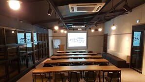 Un salón de conferencias con largas mesas y sillas, una pantalla de proyector y una pizarra.