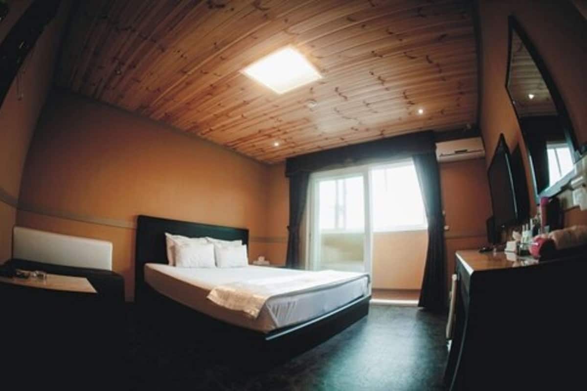 A bedroom with a wooden ceiling, a bed, a desk, and a window.