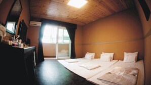 Una habitación con techo de madera, cama con ropa de cama blanca, escritorio con espejo y ventana con cortinas.