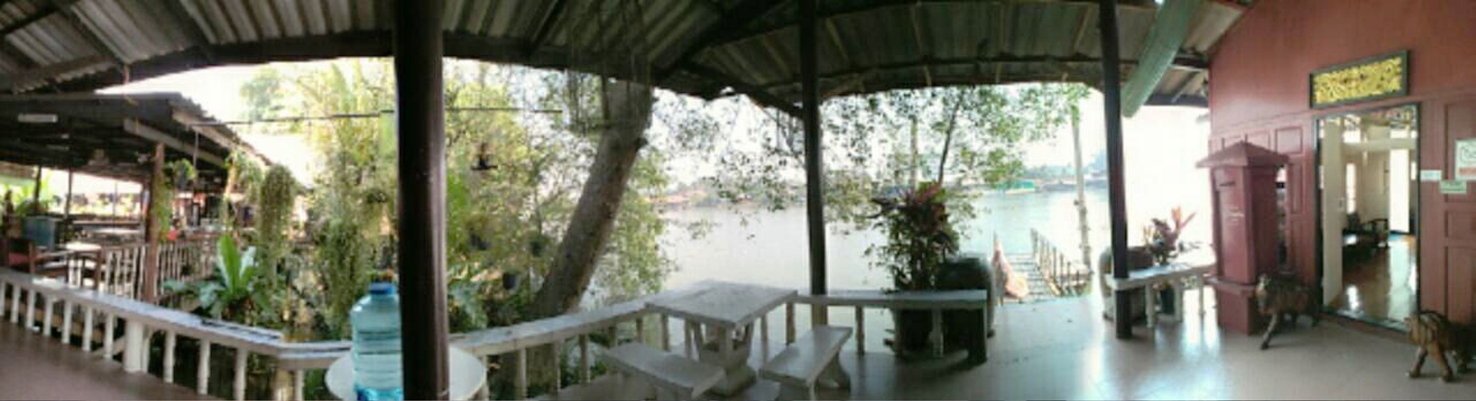 An outdoor covered area with tables and chairs, overlooking a body of water.