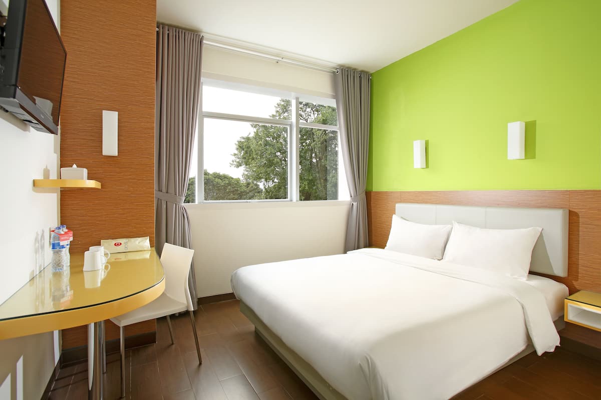 Hotelkamer met een bed, een bureau, een stoel, een raam met gordijnen en een groene wand.