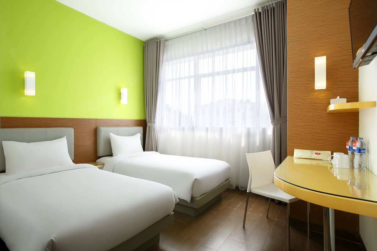Een hotelkamer met twee bedden, een tafeltje, een stoel en een raam met gordijnen.