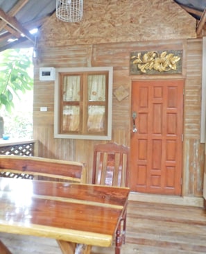 A wooden interior with a wooden door, a window with curtains, and a table with chairs. - NR Homestay (Amphawa)