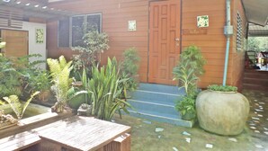 A wooden house with a brown door, a small porch, and various potted plants. - NR Homestay (Amphawa)