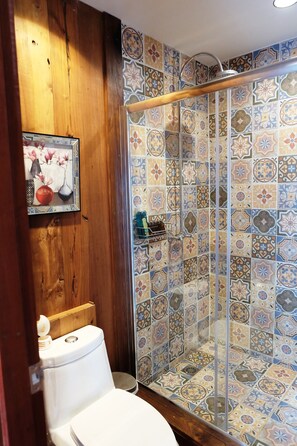 Un baño con pared de paneles de madera, cabina de ducha con azulejos y un inodoro.