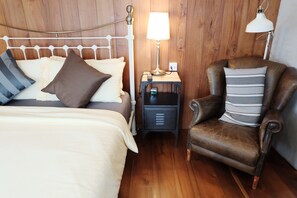 Un dormitorio con una cama, una mesita de noche, una lámpara y un sillón de cuero.