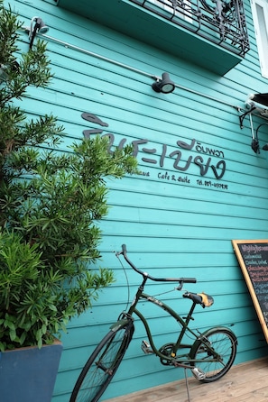 A teal building with a sign that reads "Lomita Cafe & Suite" and a contact number. A bicycle is parked in front, and a potted plant is visible to the left. - Rimrabeang Amphawa Cafe and Suite (Amphawa)