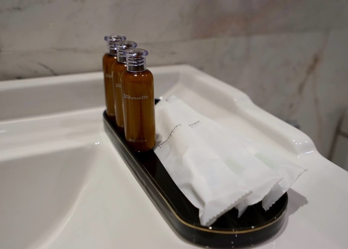 A bathroom sink with three bottles of body lotion and a tissue dispenser.