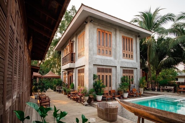 A two-story building with a pool, wooden furniture, and potted plants. - House of Passion Amphawa (Amphawa)