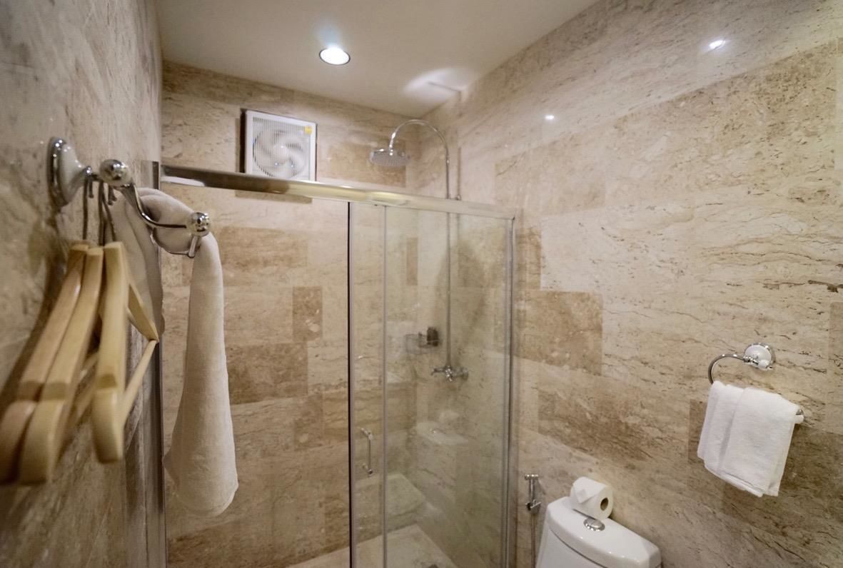 A modern bathroom with a glass-enclosed shower, marble walls, and a toilet with a paper towel dispenser.