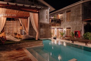 A pool area with a wooden deck, a covered seating area with cushions, and a building with multiple windows and balconies. - House of Passion Amphawa (Amphawa)