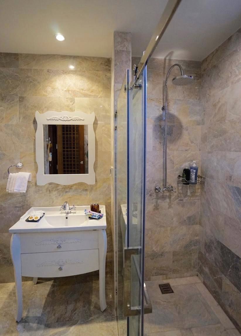 A bathroom with a glass-enclosed shower, a white vanity with a mirror, and marble walls.