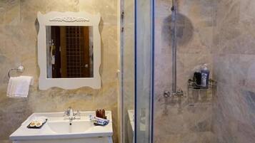 A bathroom with a glass-enclosed shower, a white vanity with a mirror, and marble walls.