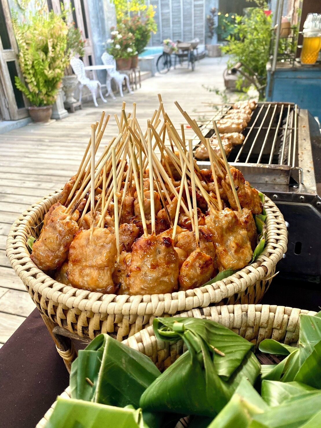 Una cesta con brochetas de pollo a la parrilla sobre una mesa, con una parrilla al fondo.