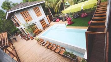 A pool area with wooden deck chairs, a small pool, and a building with large windows and a sloped roof.