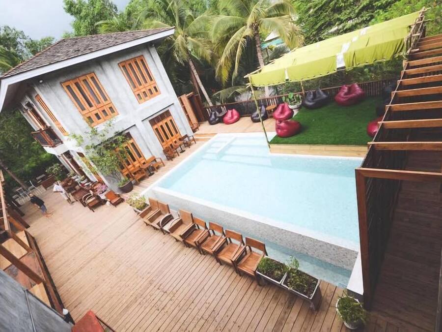 A pool area with wooden deck chairs, a small pool, and a building with large windows and a sloped roof.