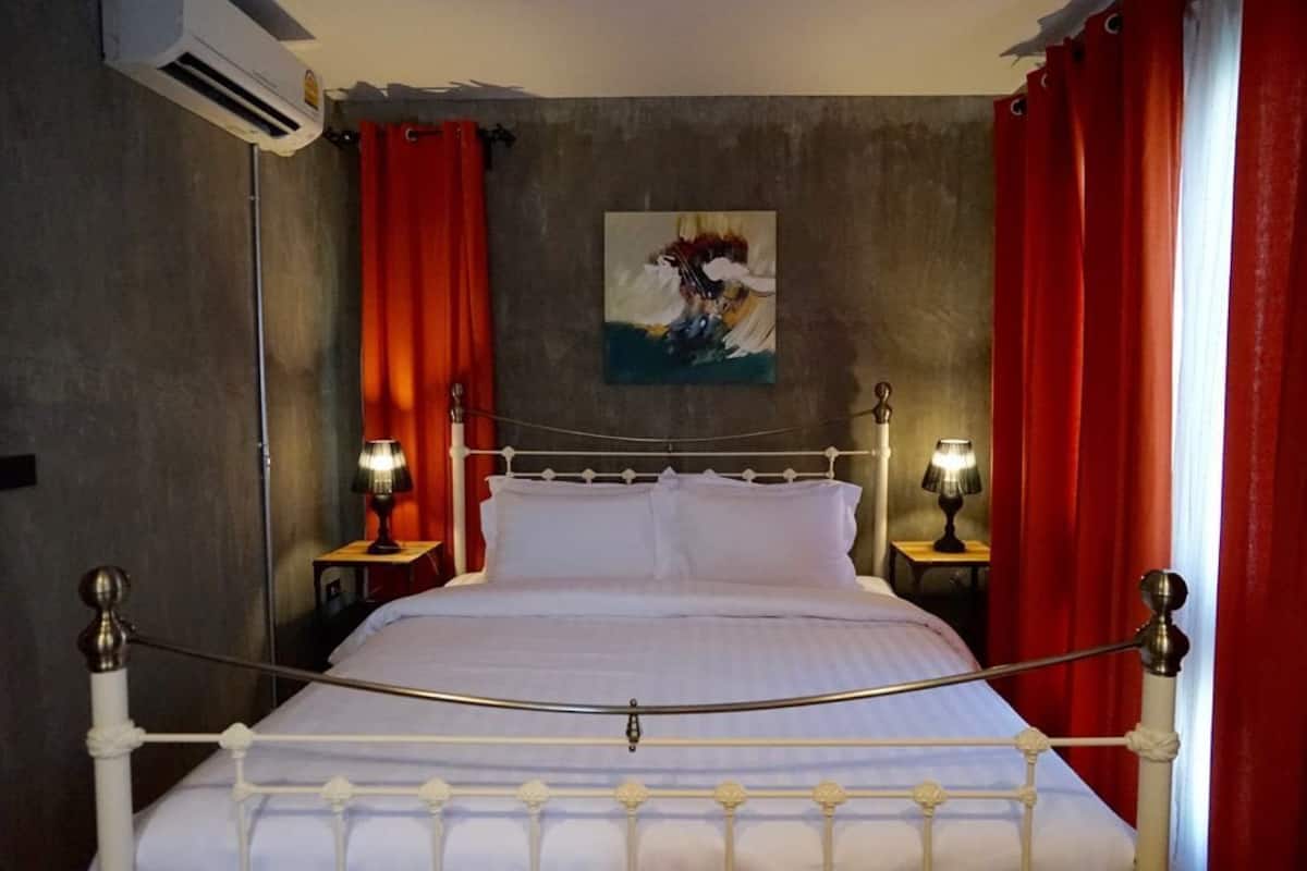 Ein Bett mit Metallgestell, zwei Nachttischlampen, ein Bild an der Wand und rote Vorhänge.