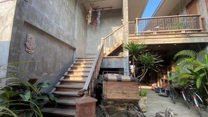 Una escalera conduce a un segundo piso con barandilla de madera, rodeada de macetas con plantas y bicicletas antiguas.