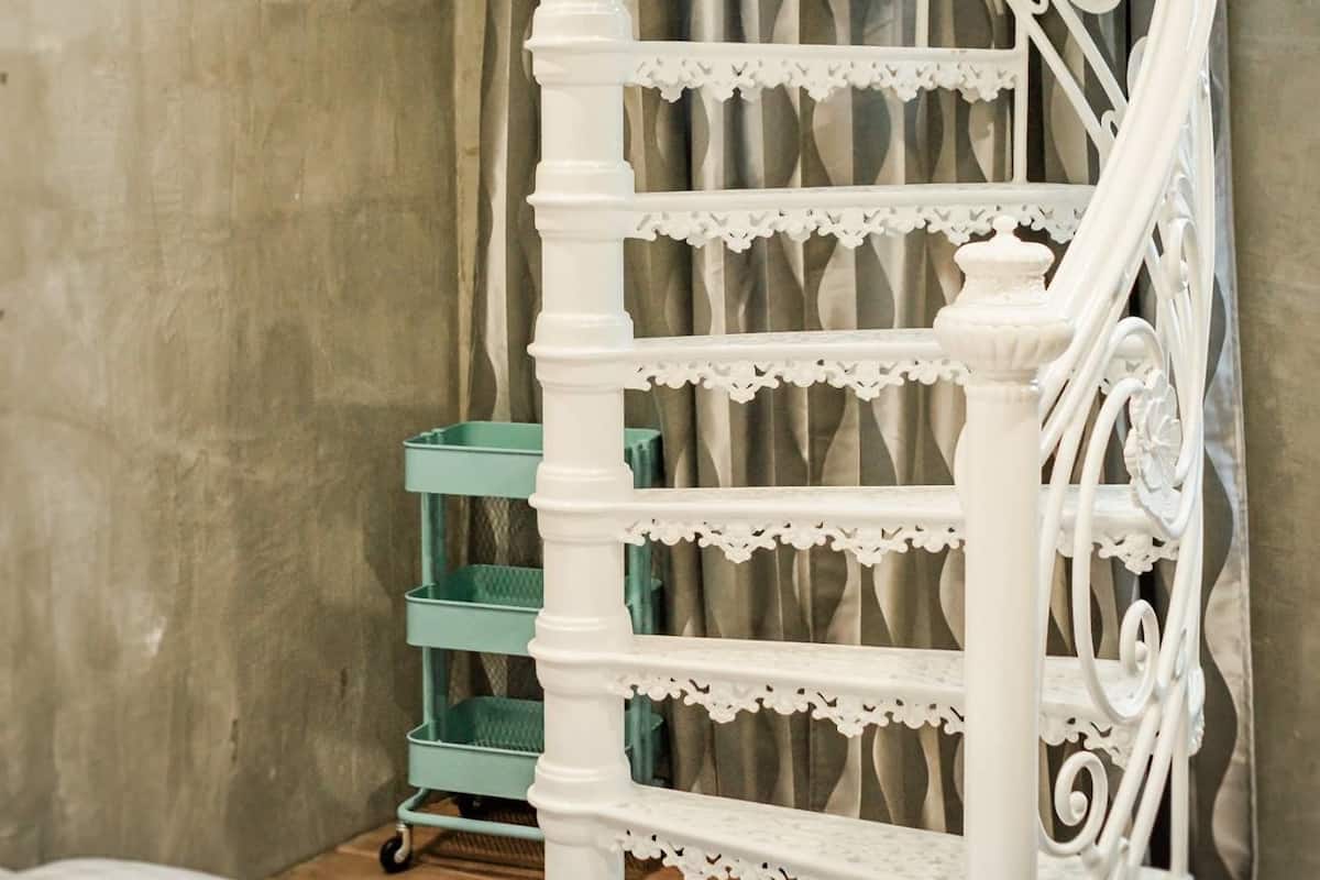 Eine Wendeltreppe mit aufwendigen weißen Geländern in einem Raum mit einer Betonwand und einem grünen Rollwagen.