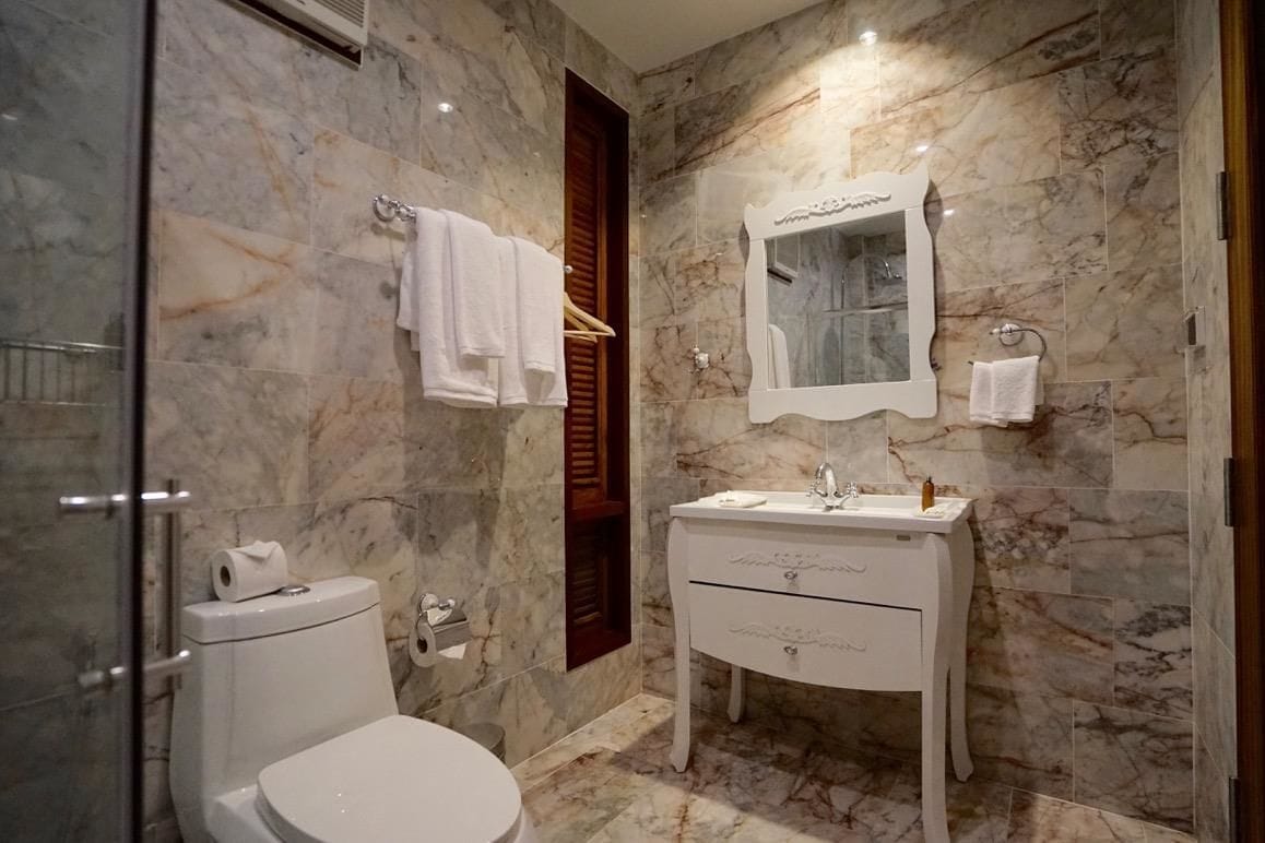 A bathroom with a marble wall, a white sink, a mirror, and a toilet.