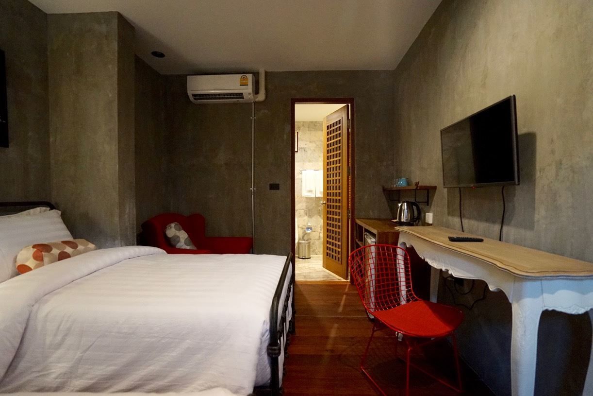 A bedroom with a bed, a red chair, a TV, and an air conditioning unit.
