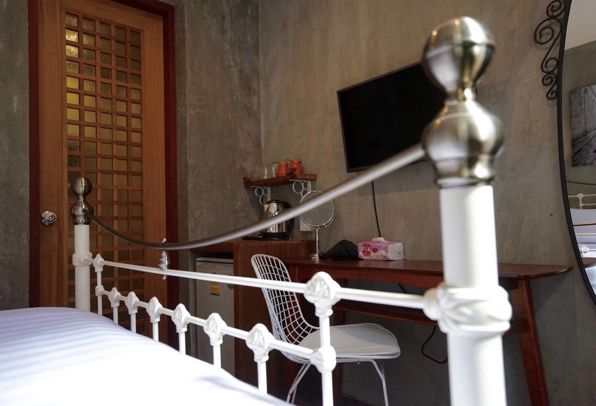Un lit avec un cadre en métal blanc, une porte en bois ornée d’un motif à carreaux et un bureau avec une chaise et un téléviseur.