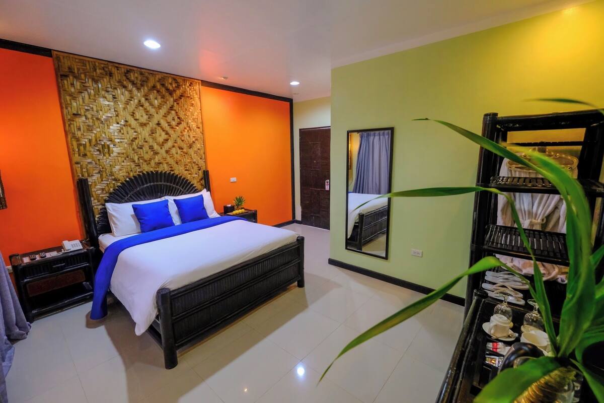 Une chambre d’hôtel avec un grand lit, une table de chevet, un miroir, une plante et une étagère avec divers objets.