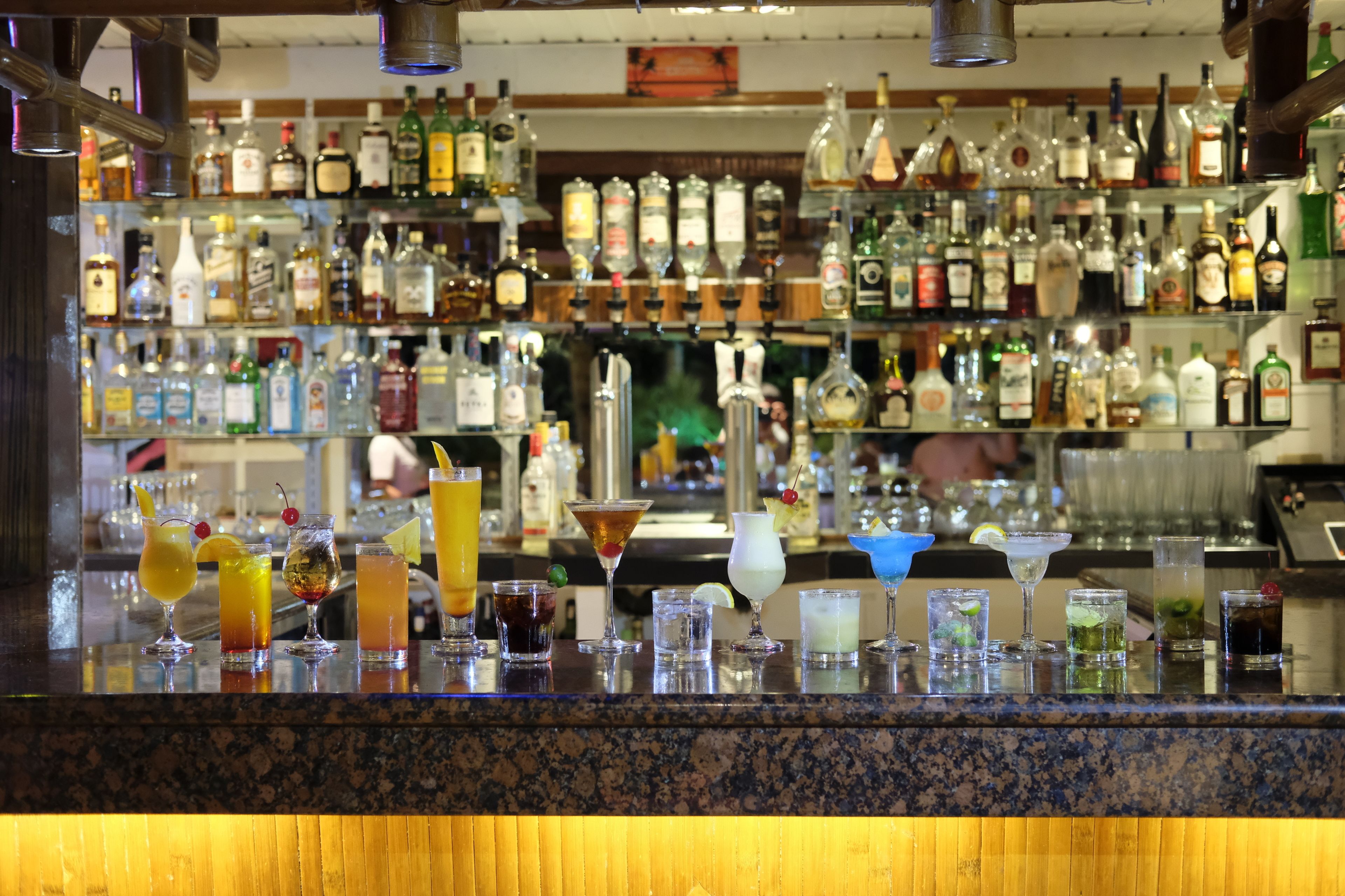 Una zona de bar con una variedad de botellas de licor y una selección de cócteles en la barra.