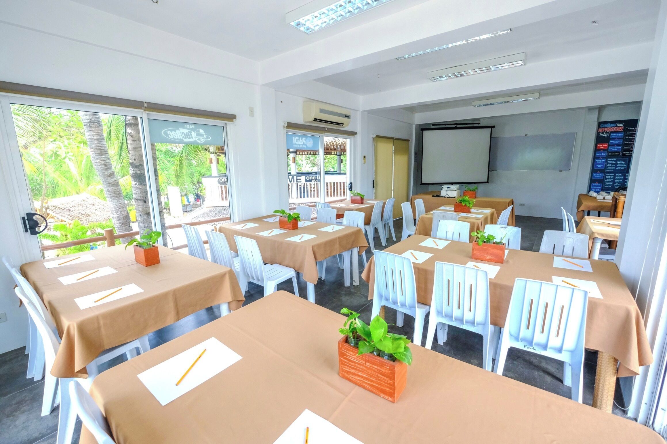 A conference room with tables set for meetings, equipped with chairs, tables, and a projector screen.