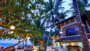 Een hotel aan het strand met palmbomen, ligbedden en een bar.