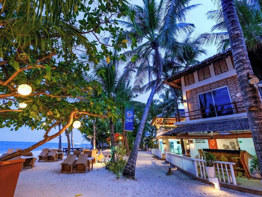 A beachfront hotel with palm trees, lounge chairs, and a bar area.