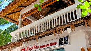 Een gebouw met twee verdiepingen, met een witte buitenkant en rieten dak. De gevel heeft een bord met 'Exotic Island Dive Resort' en een glazen displaykast.