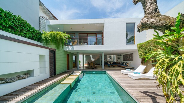 A modern house with a swimming pool, a wooden deck, and a second-story balcony. - Villa Rio (Seminyak)