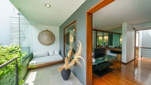 A modern living room with a glass partition, a sofa, a dining area, and a kitchen visible through the partition. - Villa Rio (Seminyak)