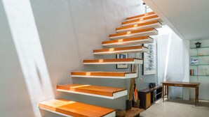 A modern staircase with wooden steps and white risers, leading to a room with a glass shelf and a wooden table. - Villa Rio (Seminyak)