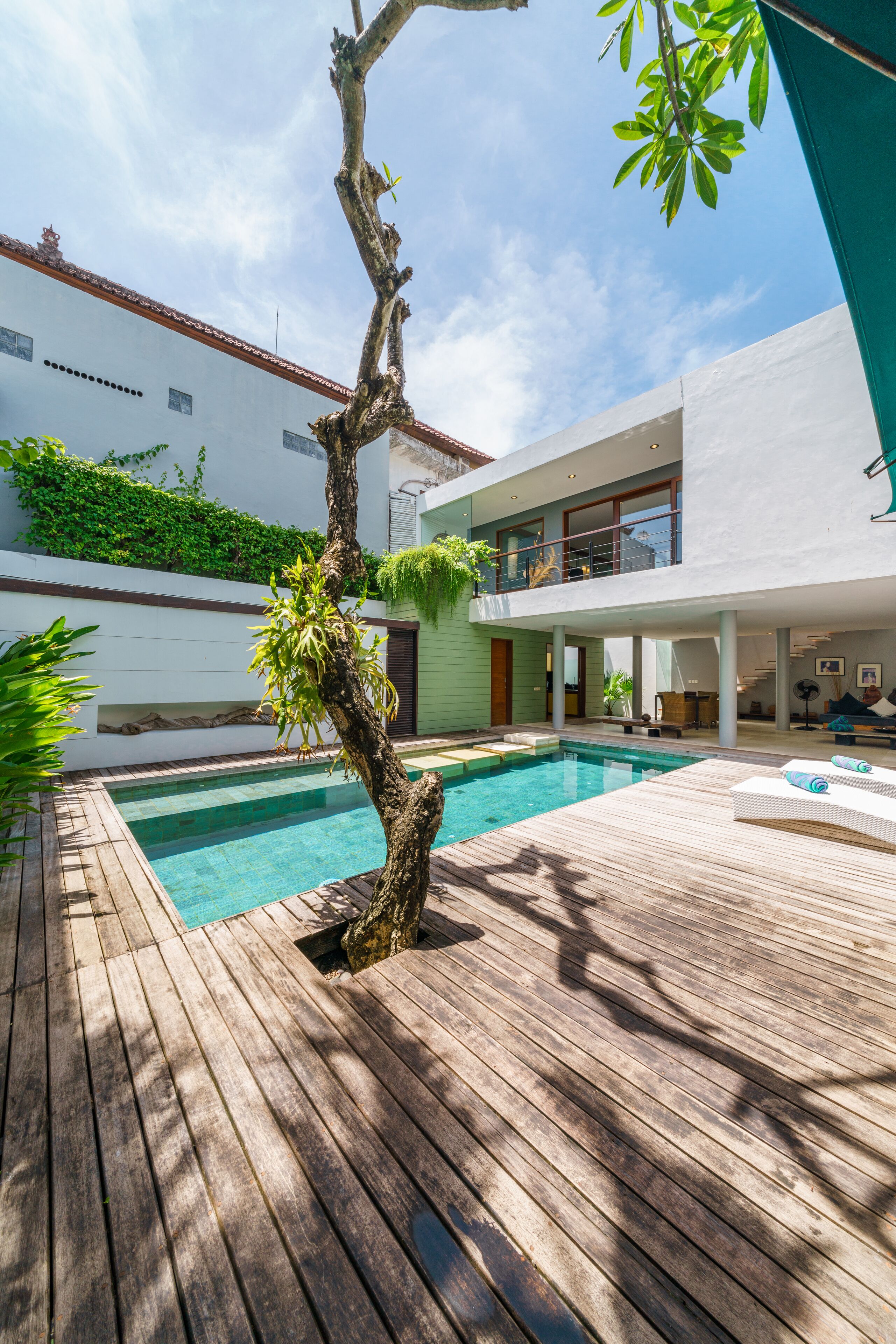 A modern house with a wooden deck, a swimming pool, and a covered outdoor area.
