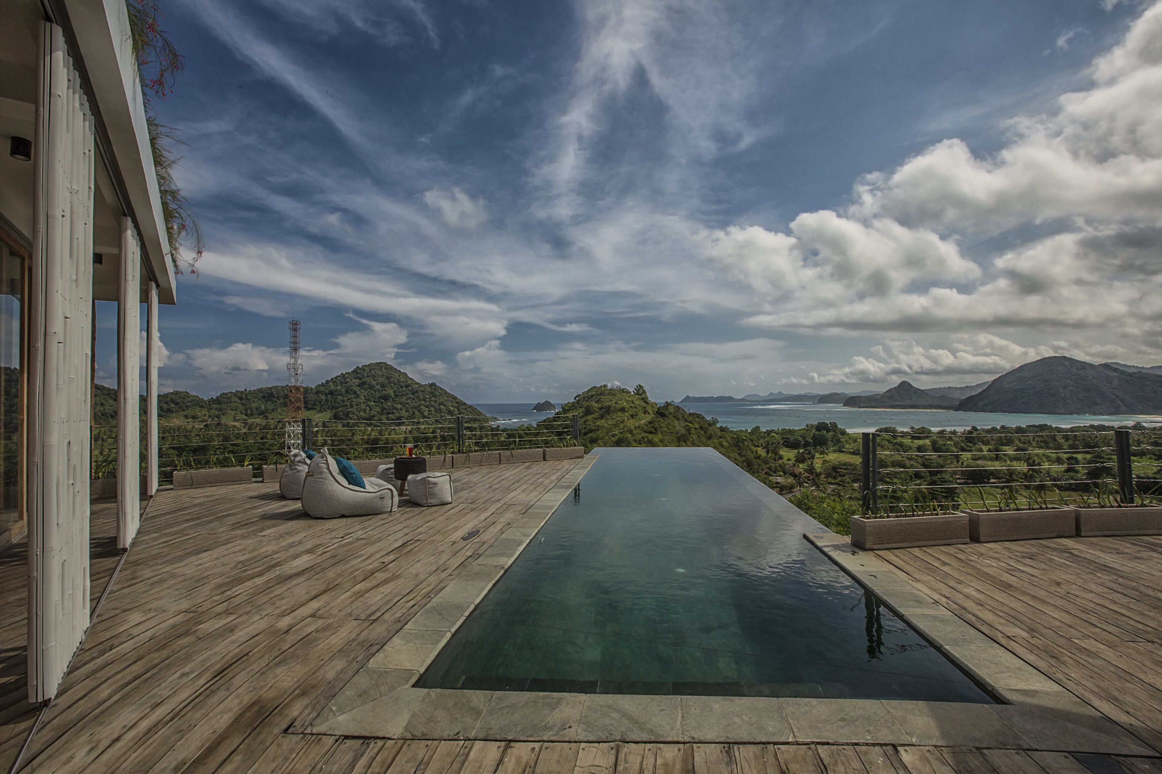 A wooden deck with a pool, outdoor seating, and a view of the ocean and mountains.
